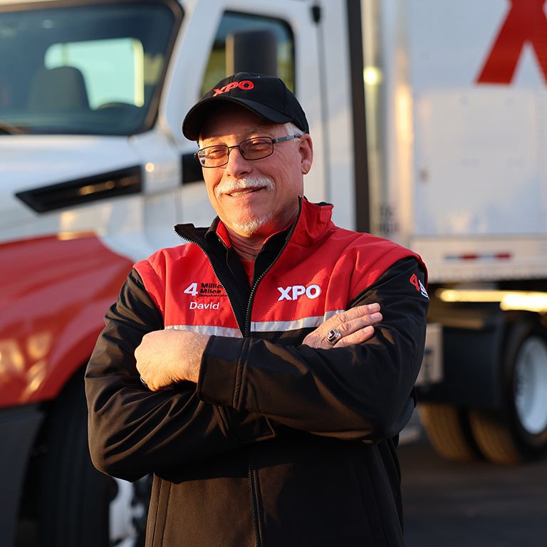 A satisfied XPO truck driver An XPO truck driver standing in front of an XPO truck